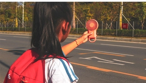 Close-up of a portable orange hand fan with a hanging loop in an outdoor scene