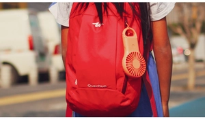Orange portable mini fan with carabiner hanging on a red backpack in outdoor setting