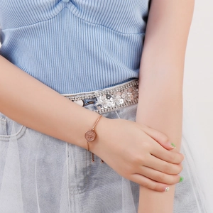 Rose gold stainless steel coin charm slider bracelet worn on wrist with elegant knit outfit