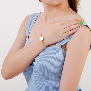 Close-up of a gold coin charm pull bracelet on a wrist with polished metallic texture