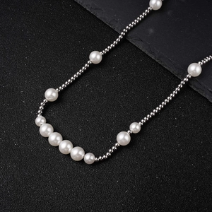 Detailed macro view of white pearls and silver steel beads on a sleek black stone surface