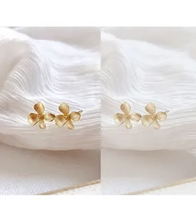 Close-up of matte gold gardenia flower earrings on white fabric background