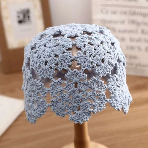 Handcrafted light blue crochet knit beanie with hollow floral pattern on a wooden stand