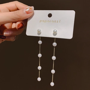 Detail view of long pearl tassel earrings with gold chains held against dark background