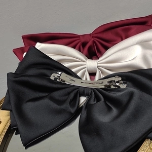 Elegant oversized satin bow hair clips in black, white, and red with metal spring clips