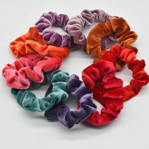 Detailed view of colorful velvet scrunchies arranged in a stack on a grey background