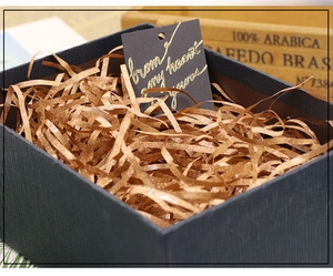 Close-up of golden glitter shredded paper filler inside a black gift box with a card