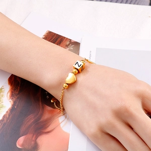 Adjustable gold heart bracelet with initial N charm on a minimalist magazine background