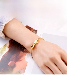 Detail of adjustable gold heart charm bracelet with R initial bead on a model wrist