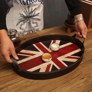 Vintage oval Union Jack tin tray with handles holding two white tea cups on a table