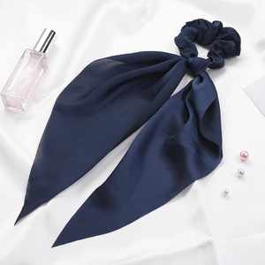 Detailed view of dark blue satin scrunchie with long ribbon bow on white silk fabric