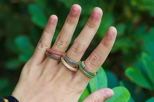 Hand model wearing five stacked micro-pave colorful zircon rings in outdoor setting