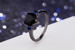 Macro detail of heart-shaped black gemstone ring with blue side stones in gunmetal setting