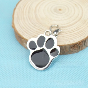 Detailed view of silver metal paw print pendant with black enamel on a wood slice