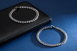 Detailed view of two silver stainless steel Cuban link bracelets on a textured background