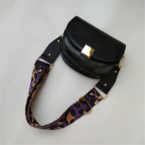 Detail of a purple leopard print wide strap attached to a black saddle bag with gold buckle