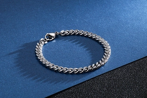Macro shot of a silver curb chain bracelet with lobster clasp on a textured background