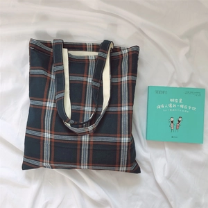 Detail of plaid canvas tote bag with thick fabric and cream webbing handles on white cloth