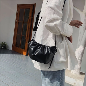 Detail of black pleated cloud bag with slim strap on a white blazer outfit