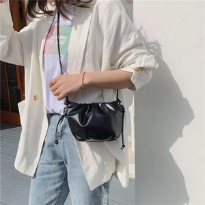 Model wearing a small black pleated drawstring shoulder bag against a white wall background