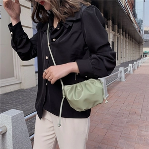 Sage green ruched cloud crossbody bag styled in a minimalist urban street setting