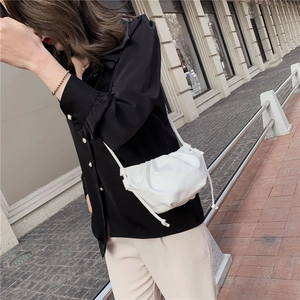 Side view of a white ruched cloud crossbody bag worn by a model in outdoor street style