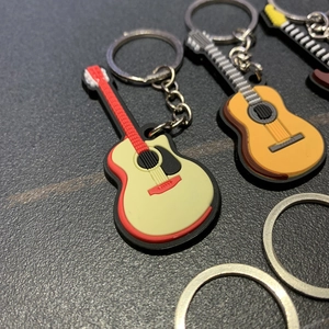 Close-up of assorted PVC guitar keychains with metal rings on a grey textured surface