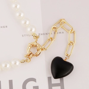 Detail of a pearl necklace with golden links and a matte black heart pendant