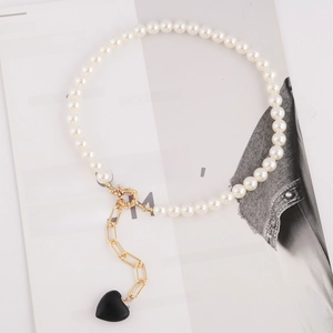 Detail of white pearl necklace featuring a gold clasp and a black 3D heart-shaped pendant