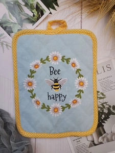 Detail of square cotton trivet with bee and daisy pattern on a white wooden background