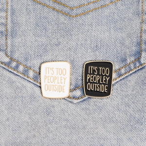 Detail of black and white enamel pins with IT'S TOO PEOPLEY OUTSIDE text on denim jeans