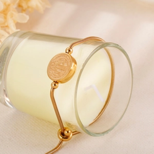 Detail of adjustable gold snake chain bracelet with embossed round coin pendant and pull ring