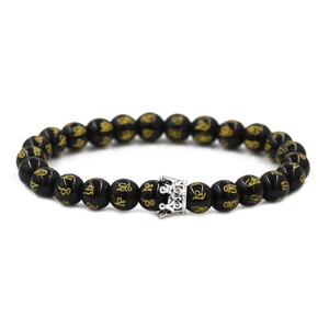 Macro detail of black onyx beads with golden mantra engraving and silver crown charm