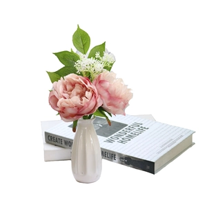 Pink artificial peony flowers in textured white ceramic vase on decorative books
