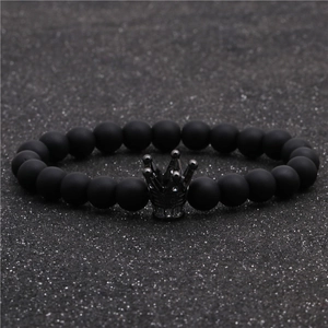 Détail d'un bracelet en perles noires mates avec un pendentif couronne sur fond scintillant