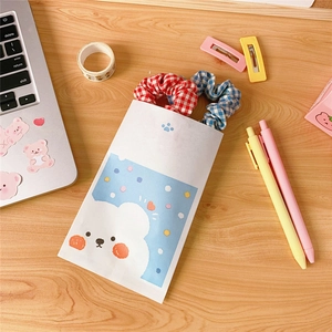 Cute bear paper gift bag with red and blue plaid hair ties on a wooden desk setup