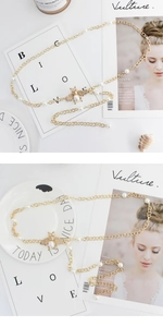 Detail of gold metal waist chain with white pearls and a dainty bee-shaped pendant