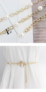 Detail of bee buckle gold chain belt with white pearls on a white dress
