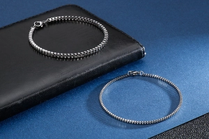 Macro shot of two silver square box chain bracelets on a black leather wallet background