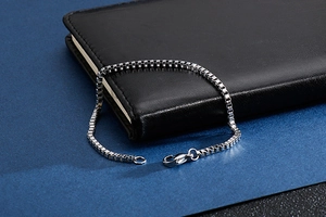 Close-up of silver stainless steel box chain bracelet resting on a black leather notebook