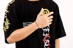 Close-up of a silver stainless steel box chain bracelet worn on a wrist with a black tee