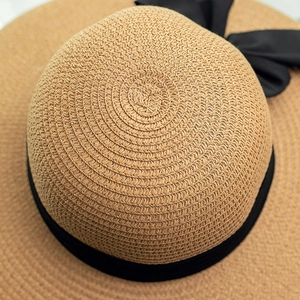 Close-up of beige straw sun hat featuring a classic black ribbon bow and spiral woven texture