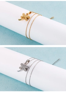 Nahaufnahme der zweilagigen Kleeblatt-Halsketten in Gold und Silber auf weißen Säulen