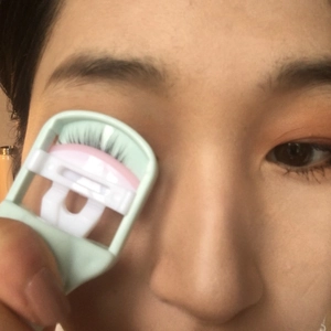 Portable light green eyelash curler with silicone pads shown in use for natural curling