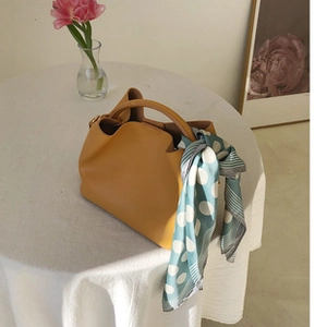 Green and white polka dot silk scarf tied on a yellow leather handbag handle detail