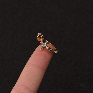 Close-up of a gold hoop earring with a colorful zircon cross pendant held on a finger