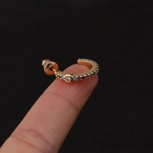 Detail of golden C-shaped earring with colored zircons and turquoise beads on fingertip