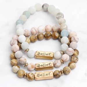 Three-piece natural stone bead bracelet set with engraved golden Belief charms on marble