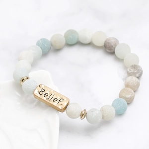 Macro detail of natural stone beaded bracelet with engraved Belief gold metal plate