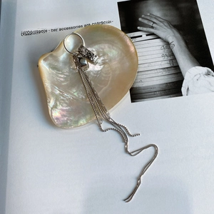 Detail of silver long tassel earrings featuring bead and curb chains on shell background